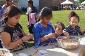 Catty Martinez, left, Shifa Gulani, Blake Hunt and Hannah Hunt string pieces of cereal together to make an edible necklace at Art in the Park in Doorknobs Park in Nederland on Saturday. Mary Meaux/The News